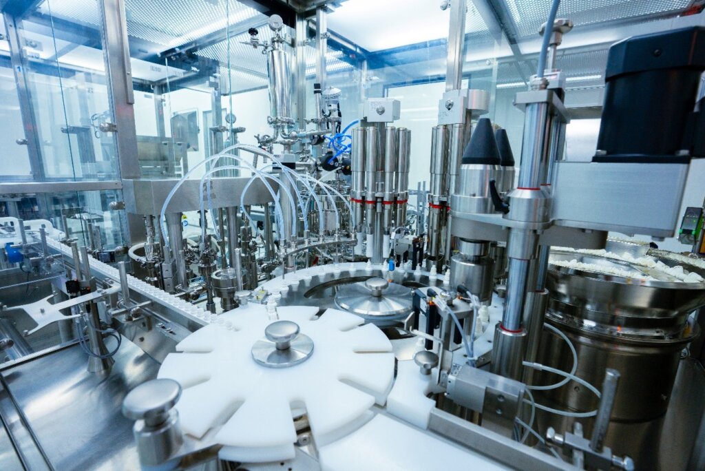 Operators loading raw materials into reactor in cleanroom, pharmaceutical manufacturing process.