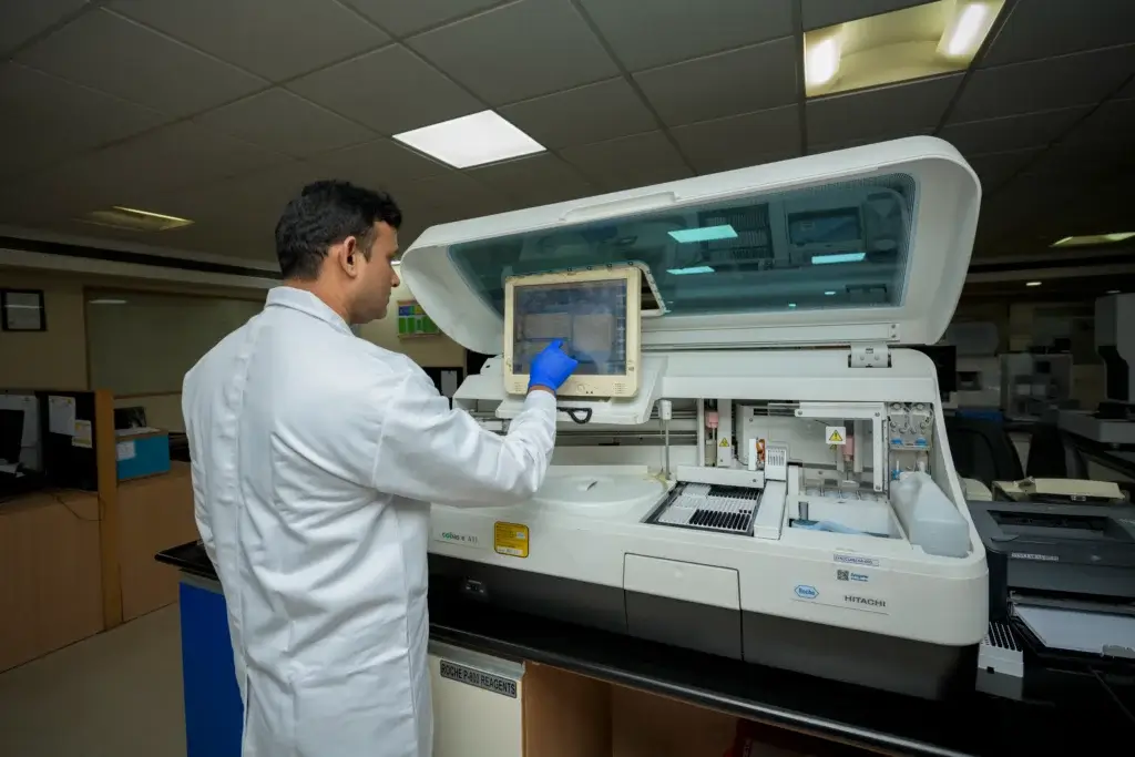 Scientist using an automated clinical analyzer with touchscreen interface for sample testing in a modern laboratory.